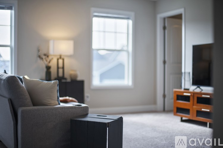 A living room with a grey couch, a black box, a wooden cabinet, and a window.