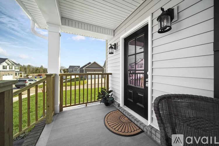 A white house with a black door and a wicker chair on the porch.