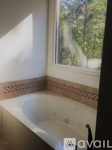 A bathroom with a tub and a window showing trees outside.