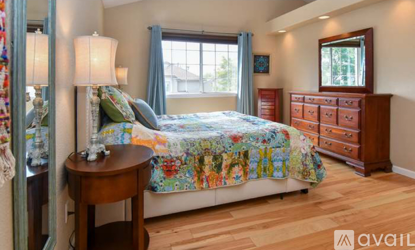A bedroom with a bed, a dresser, and a table with a lamp on it.