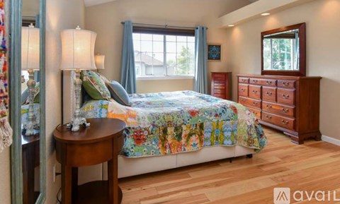 A bedroom with a bed, a dresser, and a table with a lamp on it.