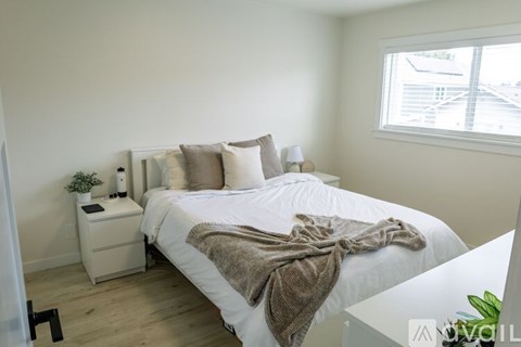 A bedroom with a white bed and a window letting in light.
