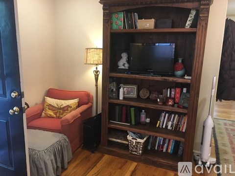 A living room with a red chair and a wooden bookshelf.