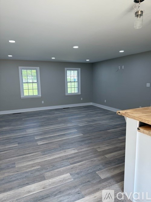 A room with wooden flooring and two windows.