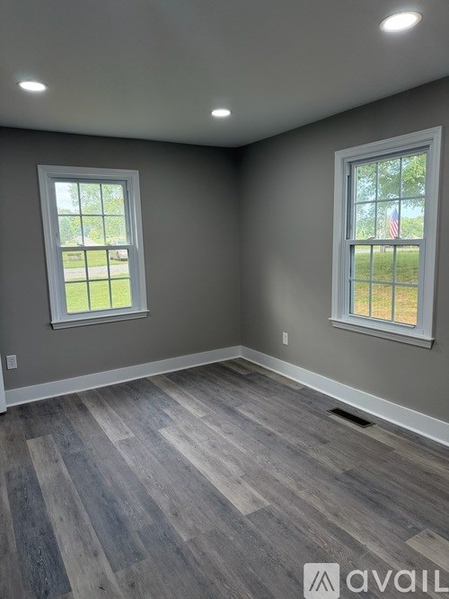 A room with grey walls and wooden flooring with two windows.