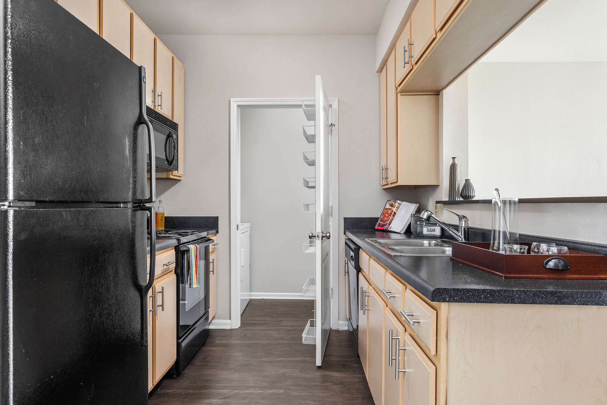 A black refrigerator is on the left in a kitchen with wooden cabinets.