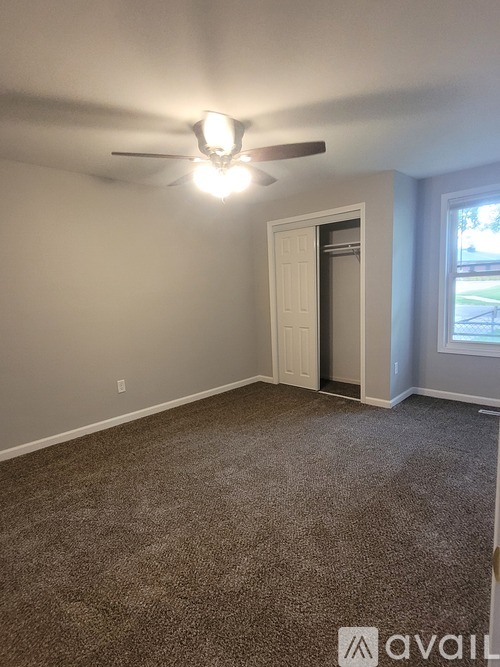 A room with a carpeted floor and a ceiling fan with a light on.
