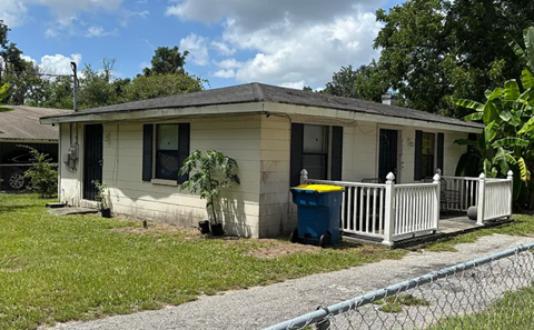 A small house with a white fence and a blue trash can.