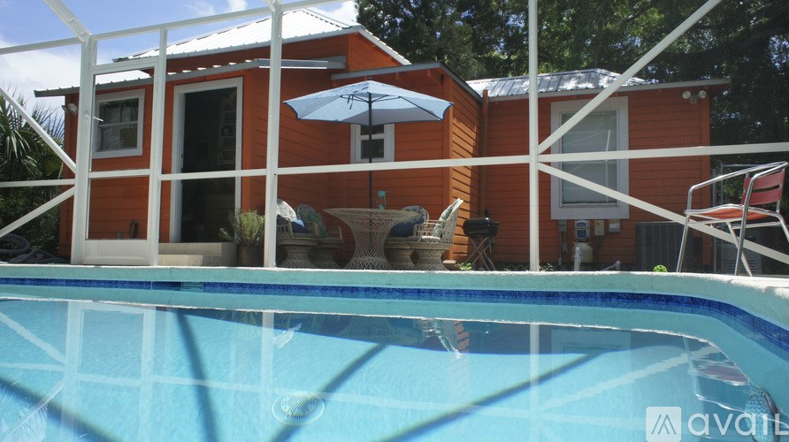 A pool in front of a red house with a white fence.