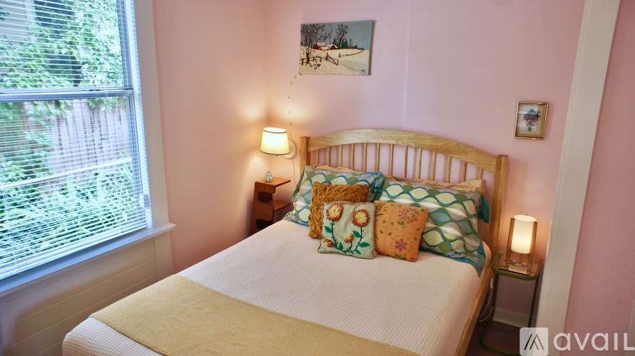 A bed with a white comforter and a yellow pillowcase is in a room with pink walls.