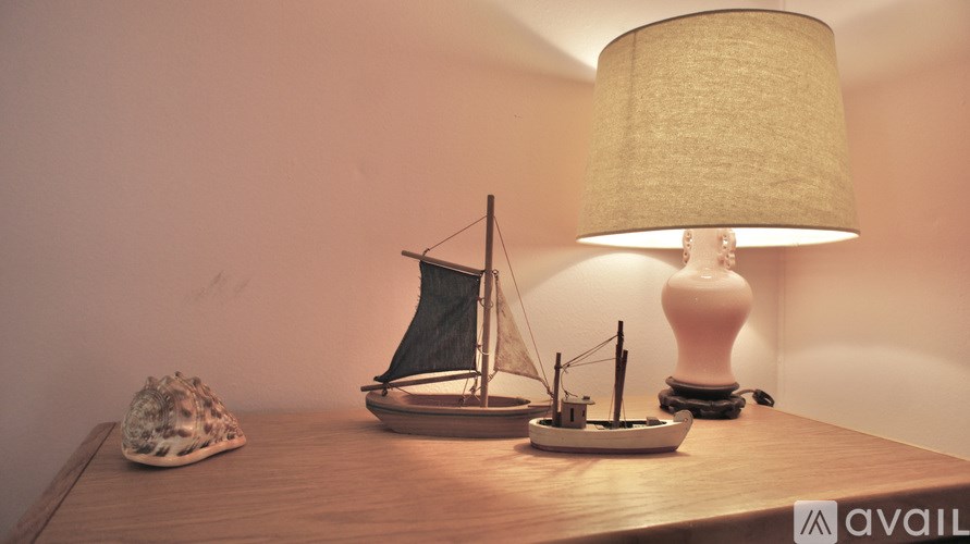 A small model sailboat sits on a table next to a lamp.