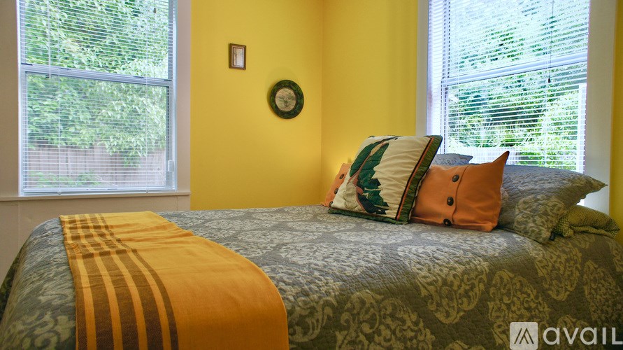A bed with a green and gold comforter and pillows in front of a window.