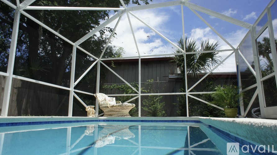 A pool surrounded by a white frame with a house and trees in the background.