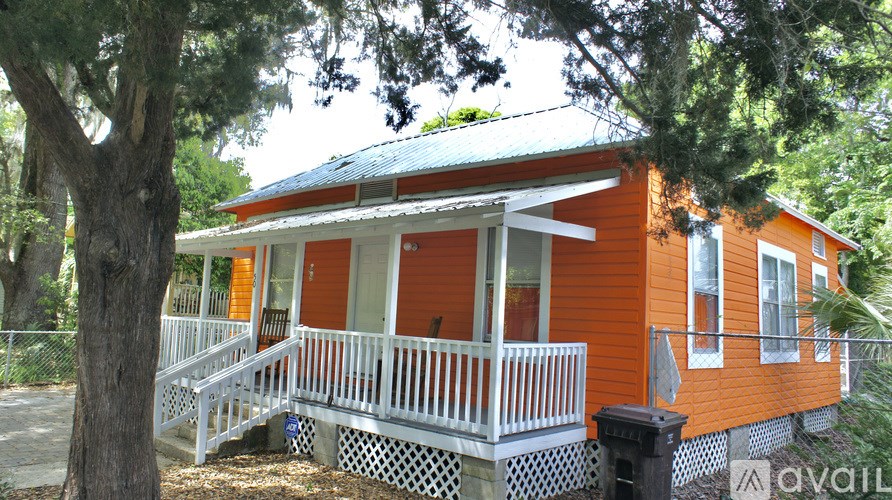 A small orange house with a porch and a tree in front.