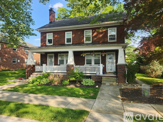 A brick house with a white porch and a tree in front.