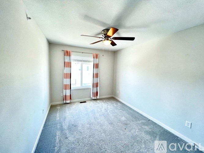 A room with a ceiling fan and a window with curtains.