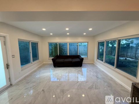 A spacious living room with a black sofa and marble flooring.