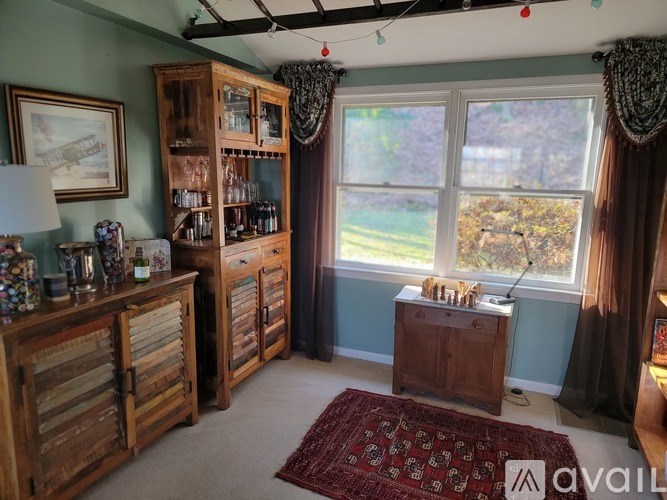 A room with a large window and a wooden cabinet filled with glasses and bottles.