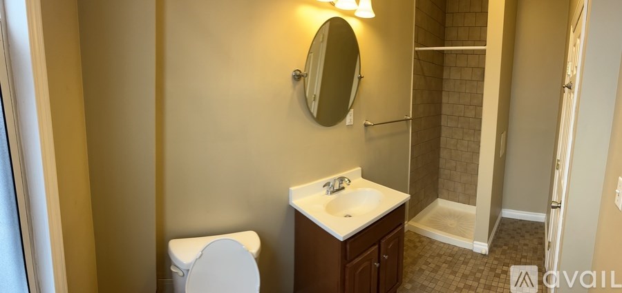 A bathroom with a toilet, sink, mirror and shower.