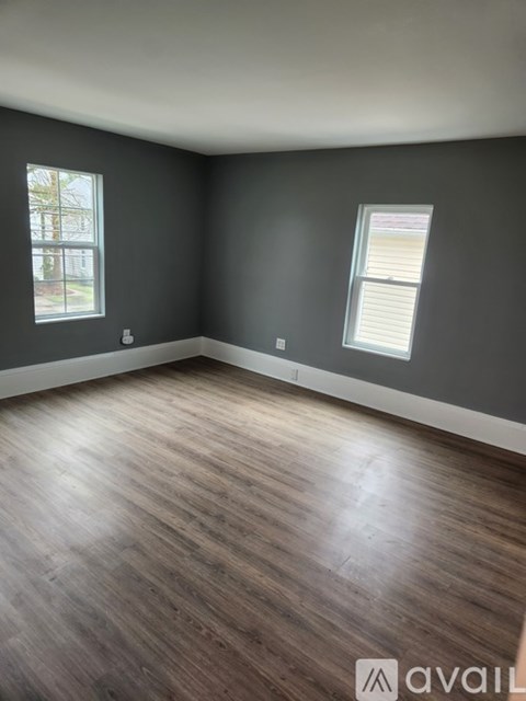 A room with wooden flooring and two windows.