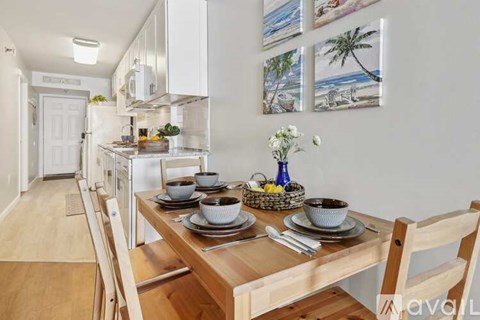 A dining table set with plates and bowls is in the foreground of a kitchen.