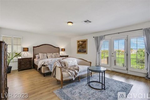 A bedroom with a large bed and a view of the backyard through the sliding glass doors.