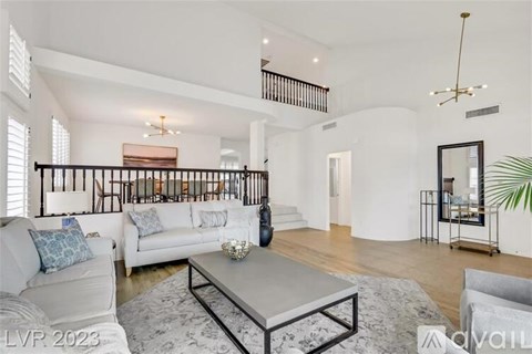 A spacious living room with a white sofa set, a grey coffee table, and a staircase with a black railing.