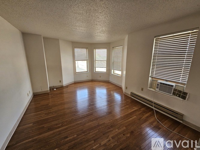 A room with wooden floors and three windows with blinds.