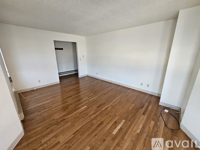A room with wooden flooring and white walls, with a doorway leading to another room.