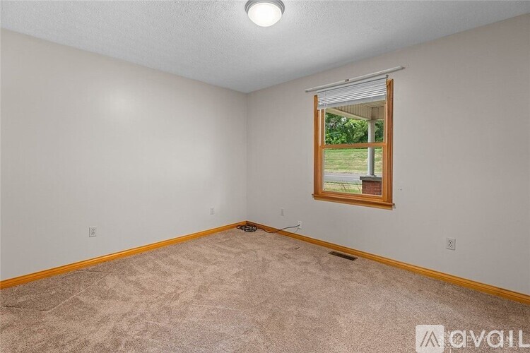 A room with a carpeted floor and a window showing a view of a green lawn.