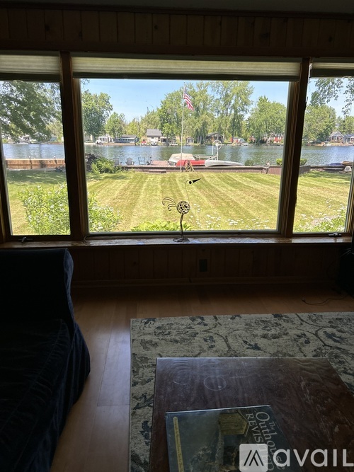 A room with a large window overlooking a grassy field and a body of water.