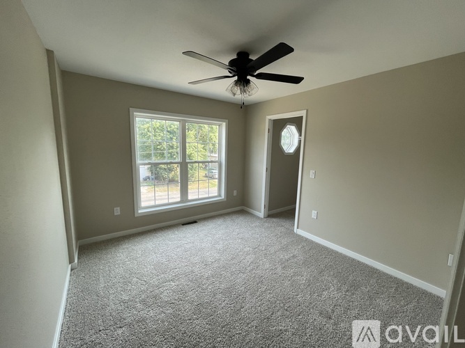 A room with a ceiling fan and a window with a view of trees.