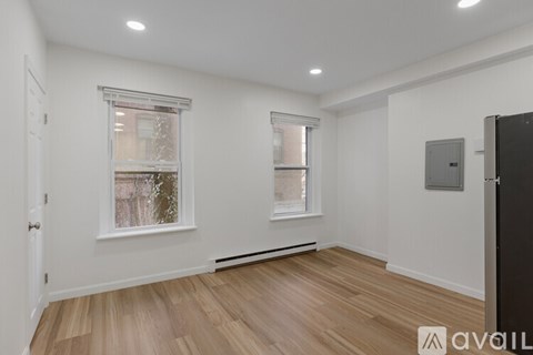 A room with wooden floors and white walls, a window with a view of trees, and a door on the right.