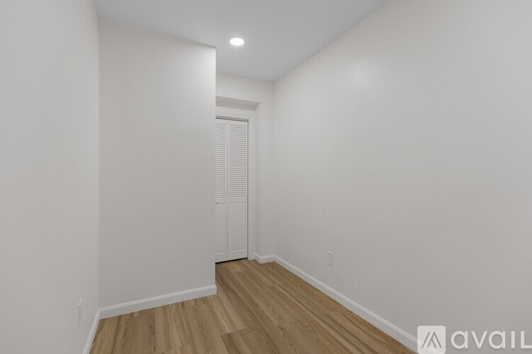 A room with a wooden floor and white walls, with a door in the background.