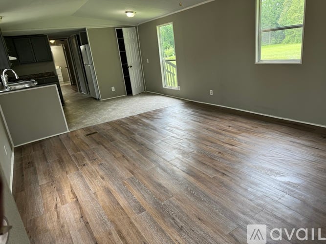 A spacious room with wooden flooring and a kitchen area to the left.