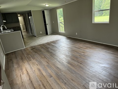 A spacious room with wooden flooring and a kitchen area to the left.