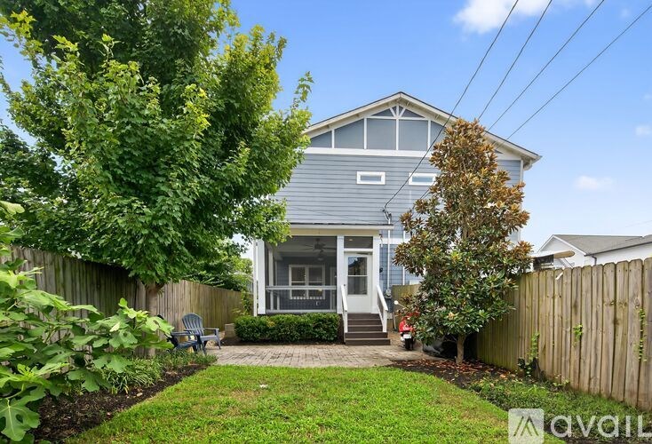 A house with a grey exterior and a white door is surrounded by a wooden fence and greenery.