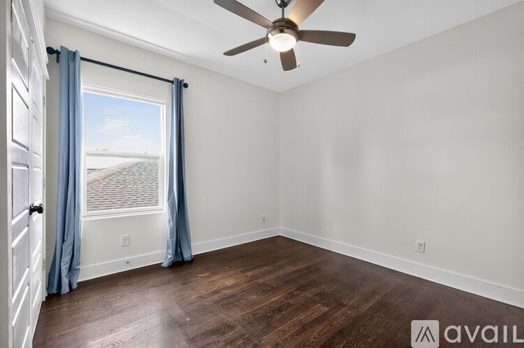 A room with a ceiling fan and a window with blue curtains.