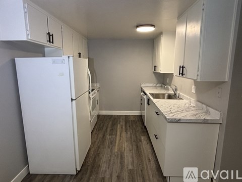 A spacious room with wood flooring and a white refrigerator.