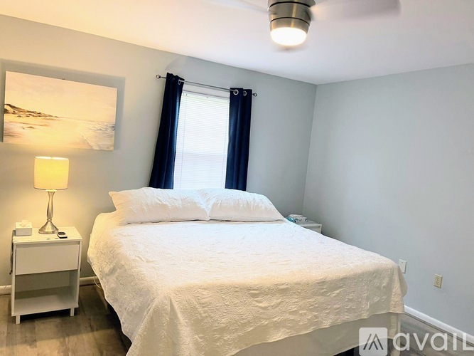 A bedroom with a white bed and a lamp on a nightstand.