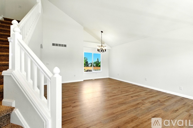 A spacious room with wooden flooring and a staircase on the left side.