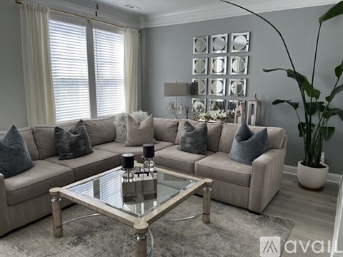 A living room with a glass coffee table and a beige sofa with grey pillows.