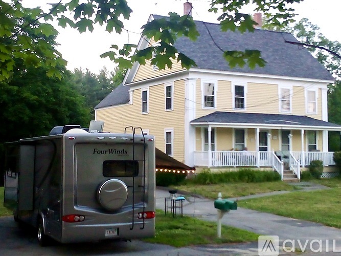 A Four Winds camper is parked in front of a yellow house.