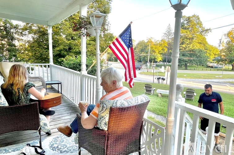 A man is sitting on a porch with an American flag in the background.