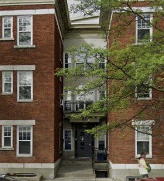 A woman in a yellow dress is walking past a red brick building.