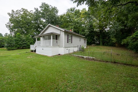 A small house with a porch is surrounded by a green lawn and trees.