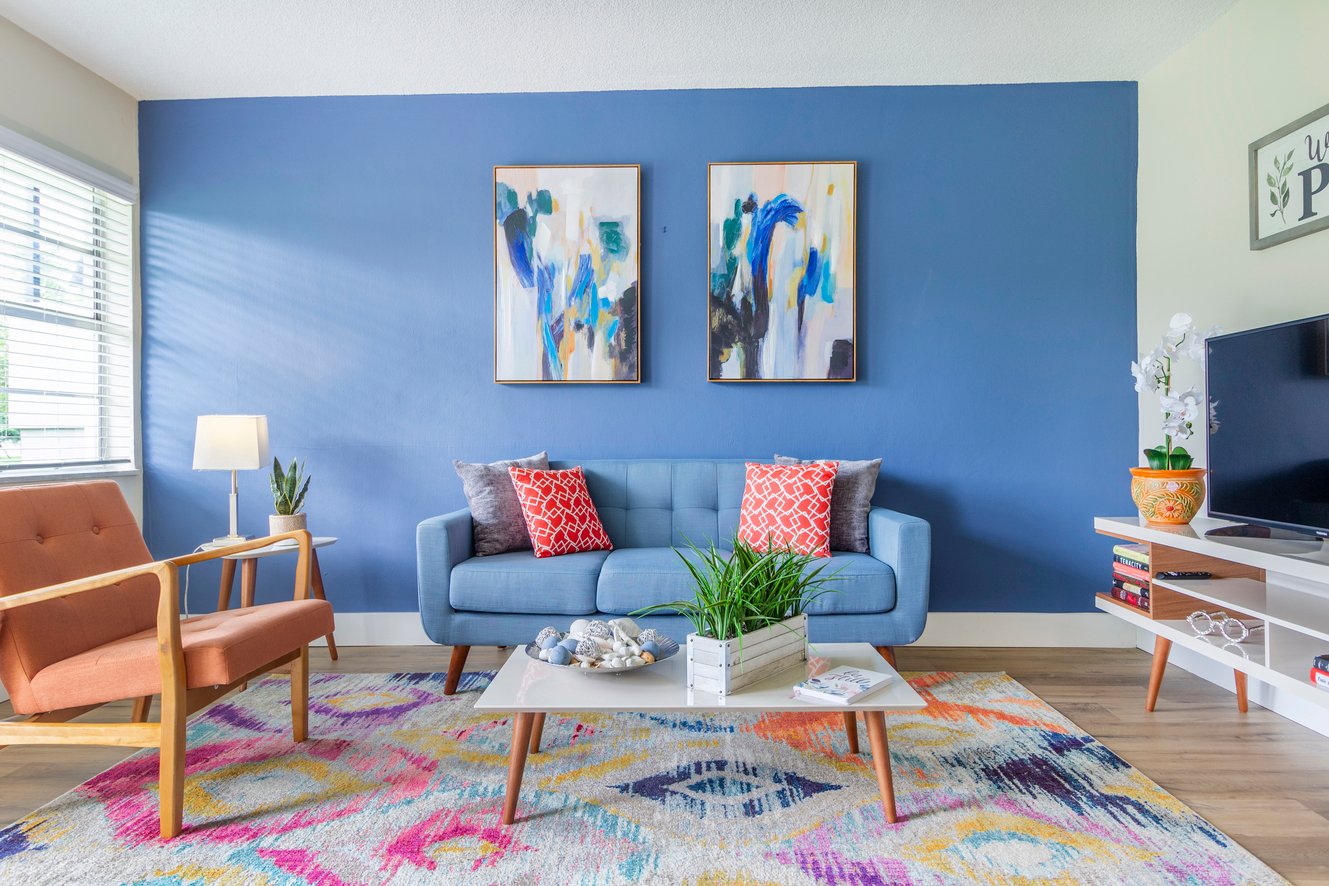 A living room with a blue couch, a wooden chair, a white coffee table, and two paintings on the wall.