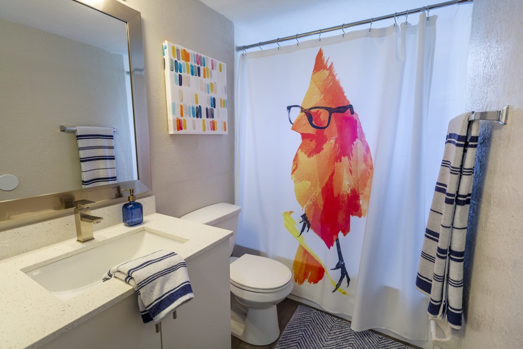 A bathroom with a white sink and a shower curtain with a bird on it.