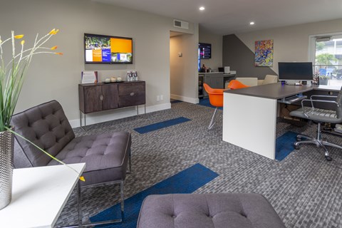 A modern office space with a white desk, black and grey chairs, and a TV mounted on the wall.