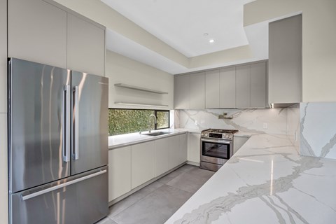 A modern kitchen with a stainless steel refrigerator and marble countertops.